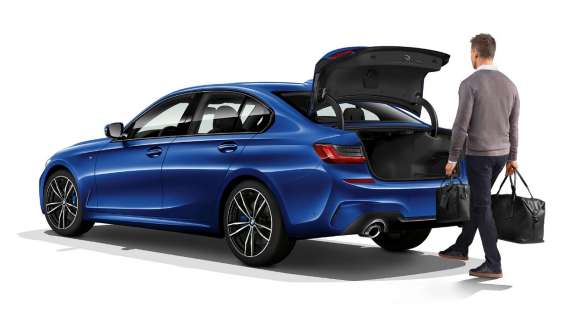 BMW 3-as Limousine, automatikus csomagtértető-működtetés. A BMW 3-as Limousine háromnegyedes hátulnézetből, a csomagtér-fedelet lábmozdulattal nyitó vezetővel.