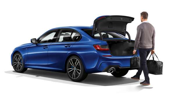 BMW 3 Limousine (G20), automatikus csomagtértető-működtetés. Egy álló, rézsútos hátulnézetből látható BMW 3 Limousine (G20), amelynek az automatikus mozgatású csomagtértetőjét a vezető lábmozdulattal nyitja.