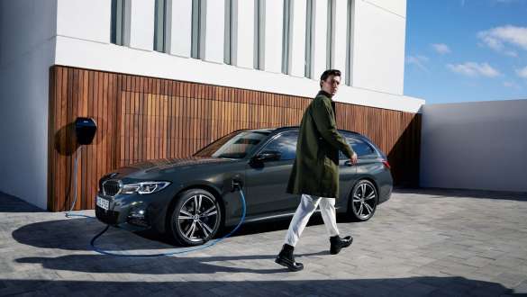 Plug-in hibrid, BMW 3 Touring, 2021, G21, egy BMW Wallbox készülékkel töltött autó rézsútos oldalnézetből Plug-in hibrid, BMW 3 Touring, 2021, G21, egy BMW Wallbox készülékkel töltőtt autó rézsútos oldalnézetből, egy modell társaságában