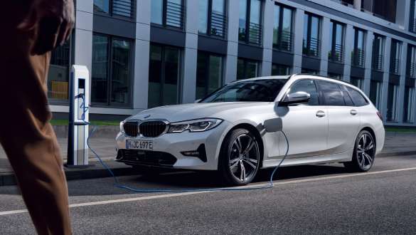 Plug-in hibrid, BMW 3 Touring, 2021, G21, egy töltés alatt álló autó rézsútos elölnézetből Plug-in hibrid, BMW 3 Touring, 2021, G21, egy épülett előtt töltés alatt álló autó rézsútos elölnézetből