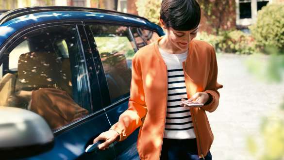 BMW Teleszerviz BMW Teleszerviz, kezében egy okostefelont tartó nő áll egy BMW ajtója mellett