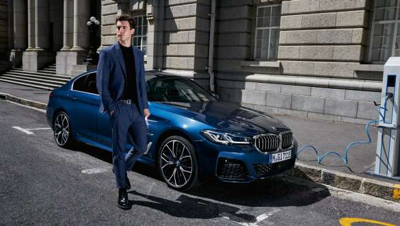 BMW 5 Limousine plug-in hibrid, 2021, G30, egy mozgó autó rézsútos elölnézetből BMW 5 Limousine plug-in hibrid, 2021, G30, egy töltés alatt álló autó rézsútos oldalnézetből, egy modell társaságában
