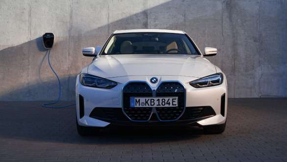 Elölnézet BMW Wallbox készülékkel, BMW i4 eDrive40, G26, 2021 BMW i4 eDrive40, G26, 2021, egy elölnézetből látható, Kristály fehér fényezésű autó áll egy házfalra felszerelt BMW Wallbox töltőállomásnál
