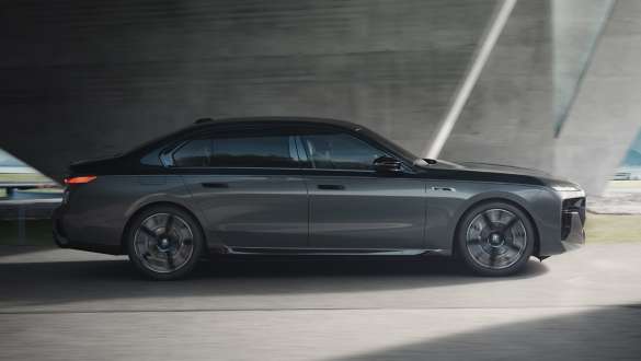 Elektromos hatótáv, BMW M760e xDrive Limousine, G70, M Performance csomag Elektromos hatótáv, BMW M760e xDrive Limousine, G70, M Performance csomag, kéttónusú BMW Individual Zafírfekete metál, BMW Individual Dravit szürke metál, egy utcán haladó autó oldalnézetből