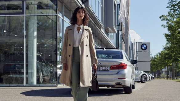 Egy nő áll egy BMW márkakereskedés előtt BMW Service Inclusive, egy nő áll egy BMW márkakereskedés előtt