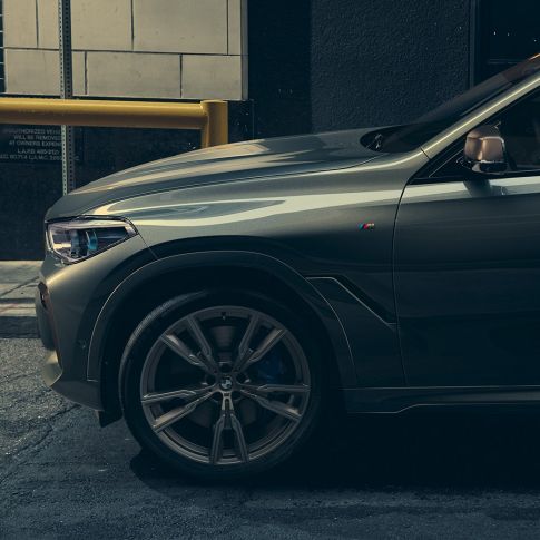 BMW X6 M50i, oldalnézet Egy BMW X6 M50i-re támaszkodó férfi, elülső oldalnézet, városi környezetben