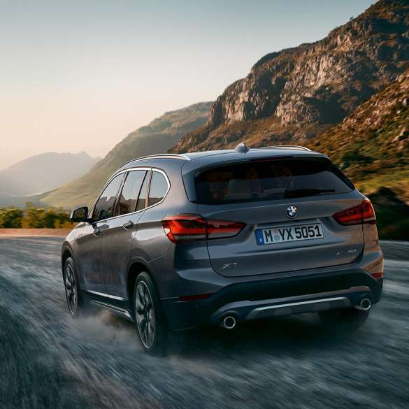 BMW X1, háromnegyedes hátulnézet. BMW X1, a mozgó autó háromnegyedes hátulnézetből, hegyvidéki tájjal a háttérben.