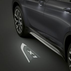 BMW X1, LED-es „X1” kivetítés. BMW X1, oldalnézet, középpontban a LED-es „X1” kivetítés.
