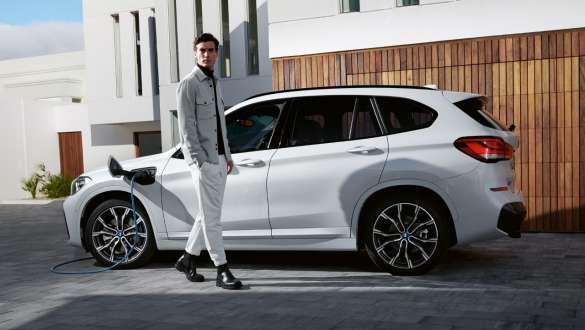 Plug-in hibrid, BMW X1 xDrive25e, F48 LCI, egy töltés alatt álló autó oldalnézetből Plug-in hibrid, BMW X1 xDrive25e, F48 LCI, egy modell társaságában látható, töltés alatt álló autó oldalnézetből