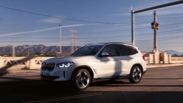 Adaptív M futómű, BMW iX3, G08, egy utcán haladó autó Adaptív M futómű, BMW iX3, G08, egy utcán haladó, Kristály fehér metálfényezésű autó rézsútos elölnézetből