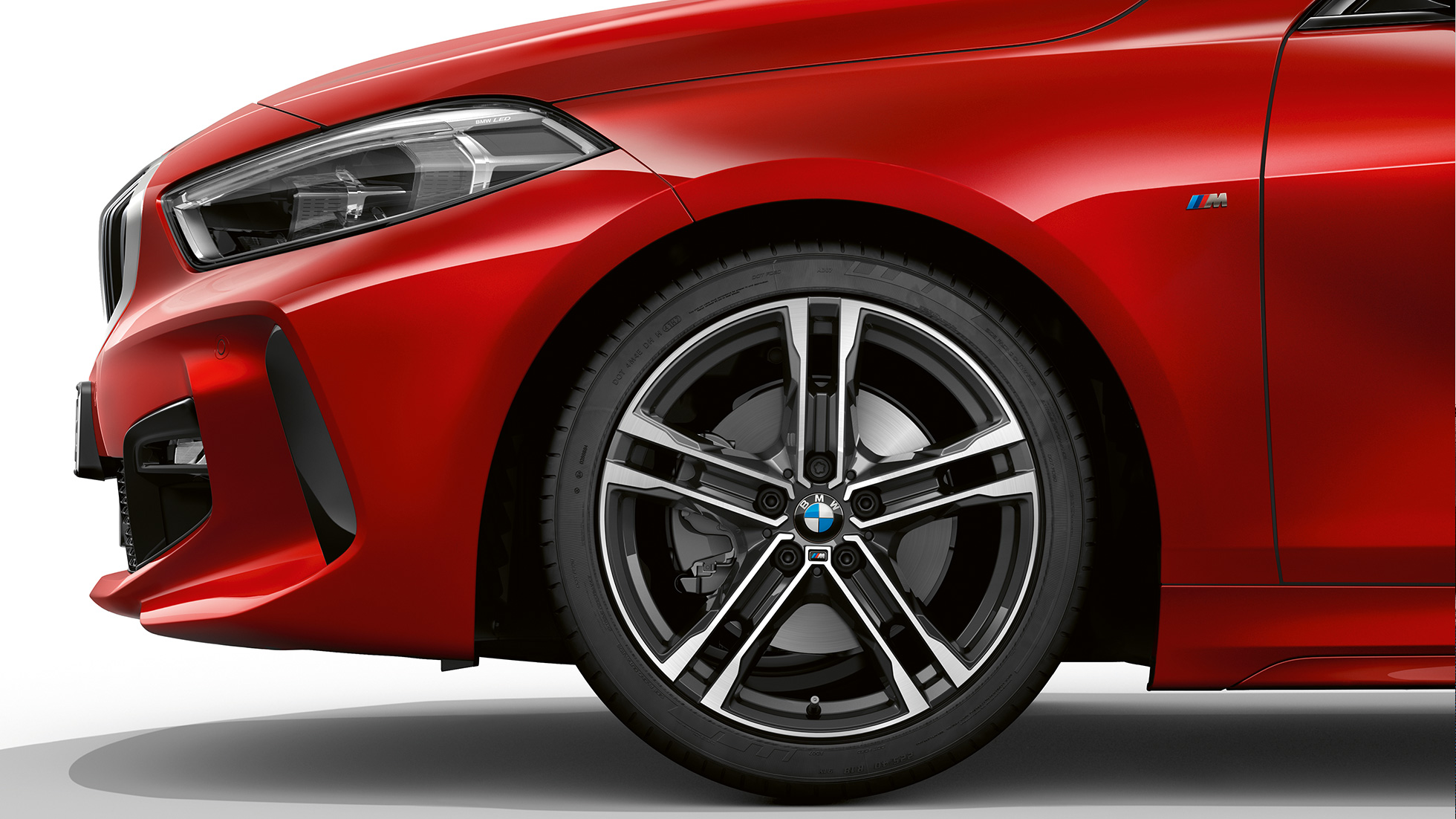 BMW 1-es, M Sport modell, rézsútos elölnézet. A BMW 1-es Melbourne vörös metál M Sport modellváltozata rézsútos elölnézetből, a 17” méretű, kétszínű, duplaküllős 550 M könnyűfém keréktárcsával.
