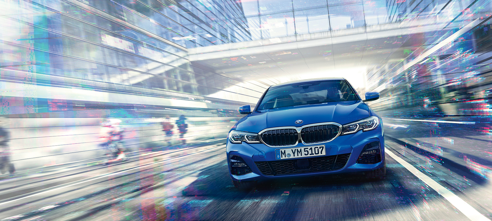 BMW 3-as Limousine szemből. Egy üvegépület alatt suhanó BMW 3-as Limousine szemből