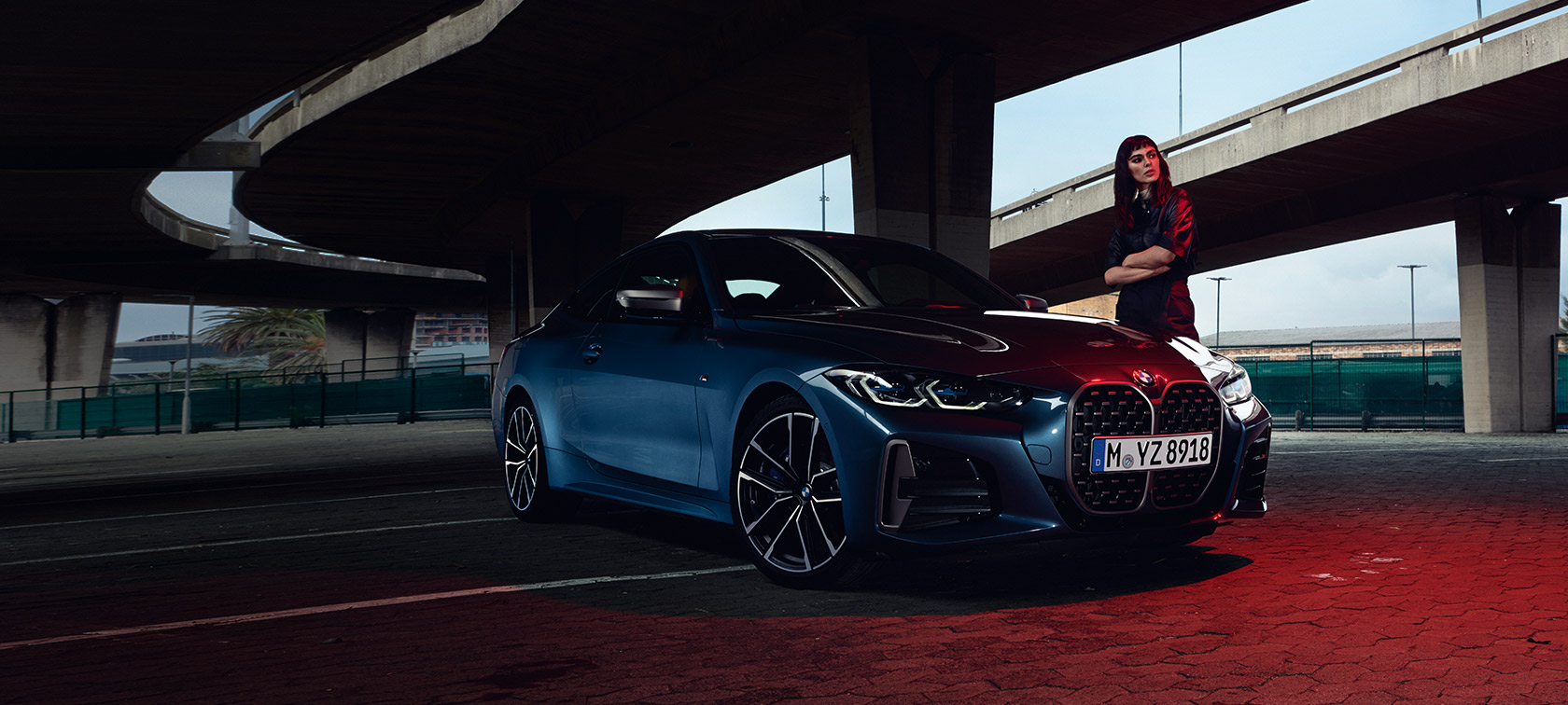 BMW 4 Coupé, G22, 2020, egy rézsútos elölnézetből látható autó egy modell társaságában