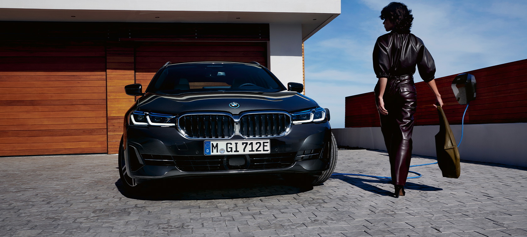 Plug-in hibrid BMW 5 Touring, 2021, G31, egy töltés alatt álló autó elölnézetből Plug-in hibrid BMW 5 Touring, 2021, G31, egy töltés alatt álló autó elölnézetből, egy modell társaságában