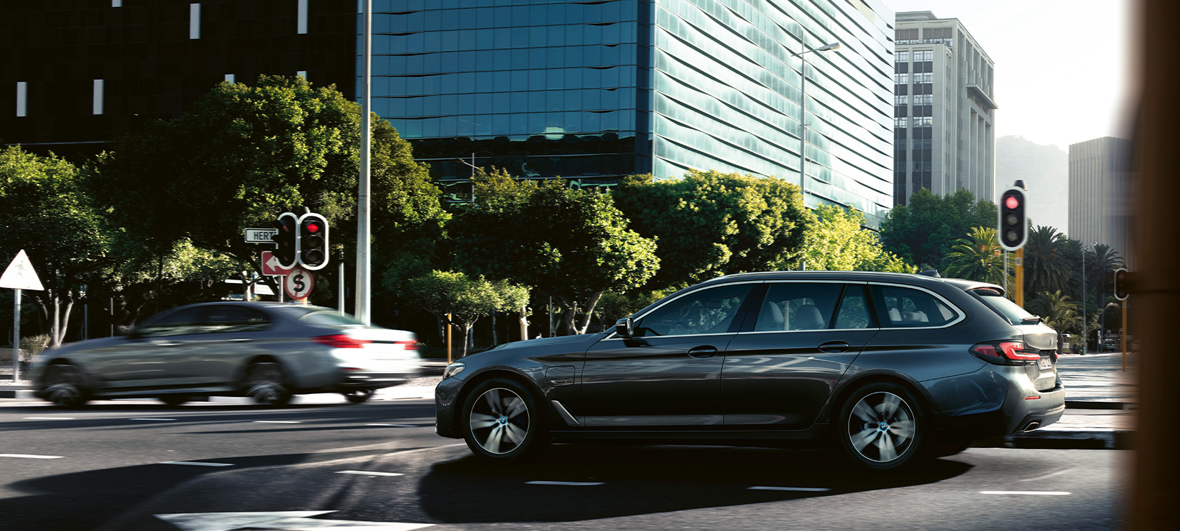 BMW 5 Touring, G31, egy mozgó autó BMW 5 Touring, G31, Facelift 2020, egy városban haladó, Sophisto szürke fényezésű autó oldalnézetből
