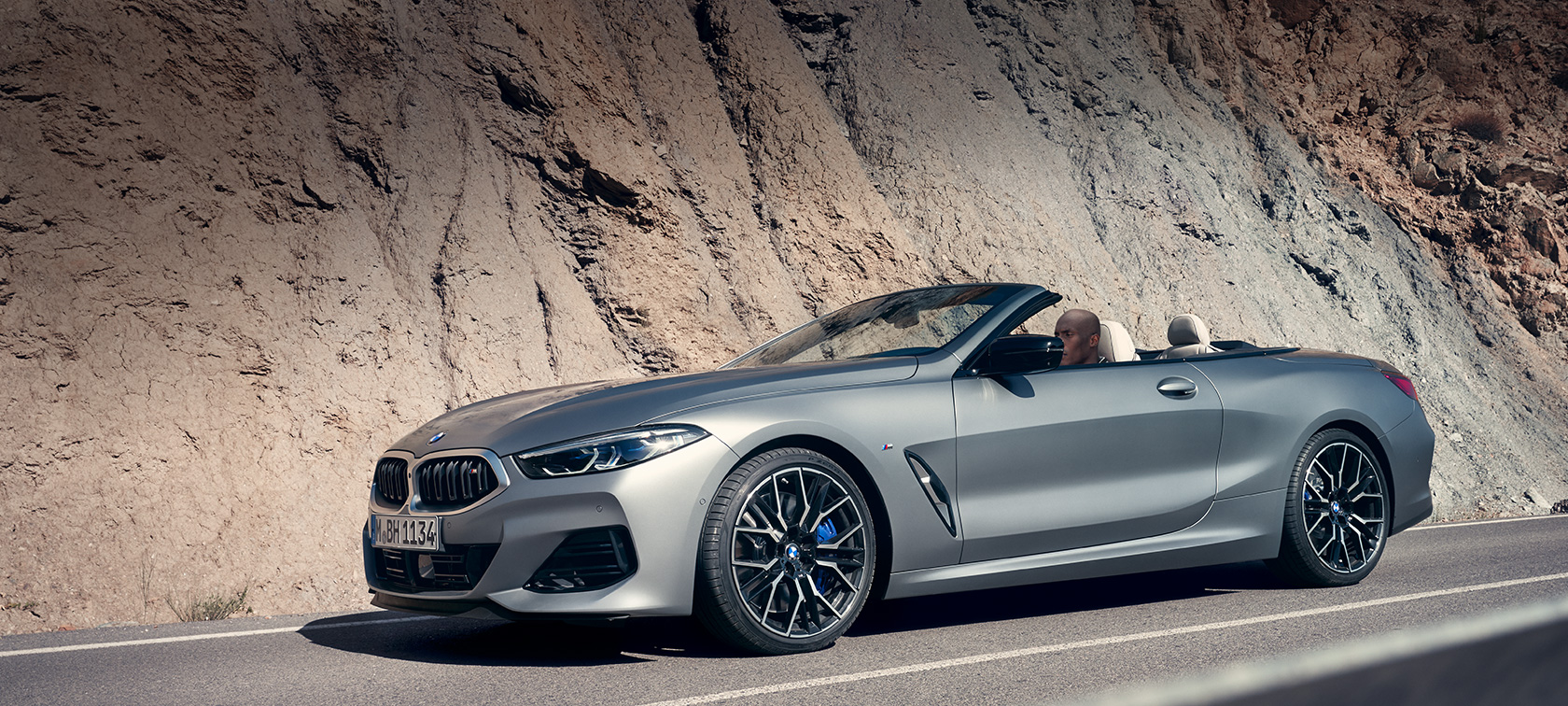 BMW 8 Cabrio, G14 LCI, Facelift 2022, BMW M850i xDrive Cabrio, egy épület előtt álló, BMW Individual Frozen Pure szürke metálfényezésű autó rézsútos oldalnézetből BMW 8 Cabrio, G14 LCI, Facelift 2022, BMW M850i xDrive Cabrio, egy épület előtt álló, BMW Individual Frozen Pure szürke metálfényezésű autó rézsútos oldalnézetből