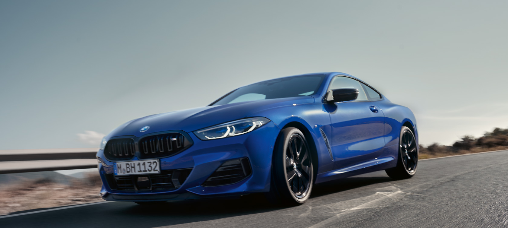 BMW 8 Coupé, G15 LCI, Facelift 2022, BMW M850i xDrive, M Portimao kék metál, alsó elölnézet BMW 8 Coupé, G15 LCI, Facelift 2022, egy vidéki úton haladó, alsó elölnézetből látható, M Portimao kék metálfényezésű BMW M850i xDrive hegyekkel a háttérben