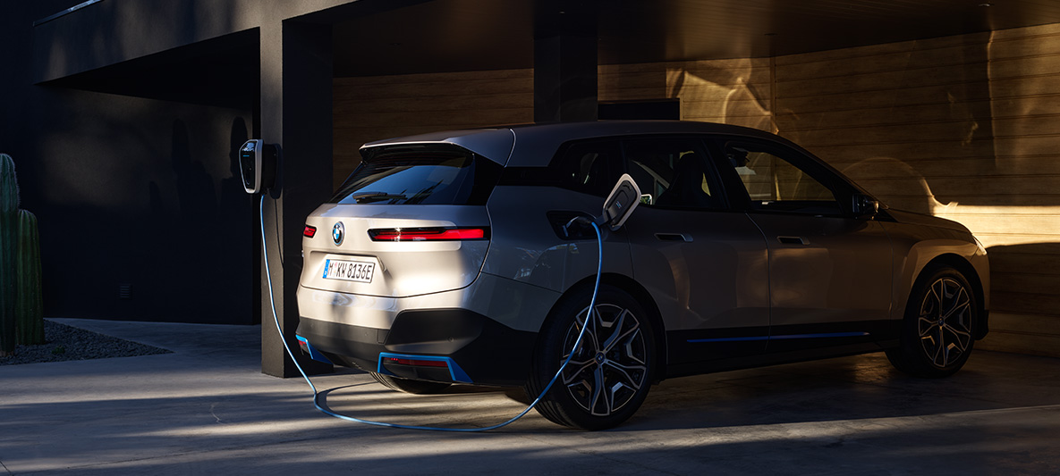 BMW iX, egy BMW Wallboxhoz csatlakoztatott autó rézsútos hátulnézetből BMW iX, Kashmir ezüst, i20, egy BMW Wallboxhoz csatlakoztatott autó rézsútos hátulnézetből