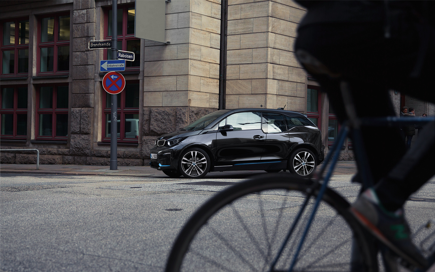 BMW i3s, i01, 2018, oldalnézet BMW i3s, i01, 2018, Fluid fekete BMW i kék kiemeléssel, egy városi környezetben haladó autó oldalnézetből