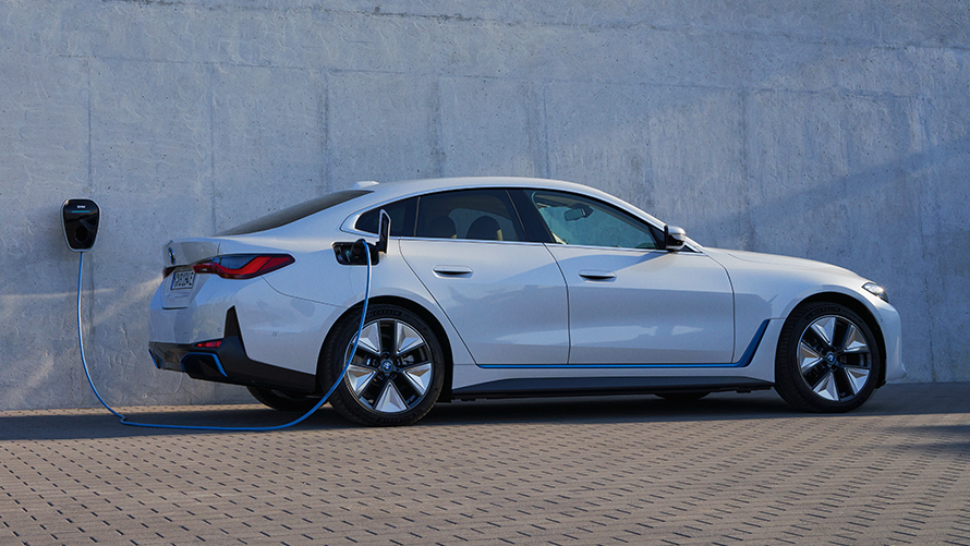 Oldalnézet BMW Wallbox készülékkel, BMW i4 eDrive40, G26, 2021 BMW i4 eDrive40, G26, 2021, egy oldalnézetből látható, Kristály fehér fényezésű autó áll egy házfalra felszerelt BMW Wallbox töltőállomásnál