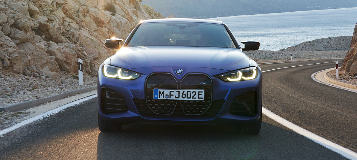Egy mozgó autó elölnézetből, BMW i4 M50, G26, 2021 BMW i4 M50, G26, 2021, egy úton haladó, M Portimao kék metálfényezésű autó elölnézetből