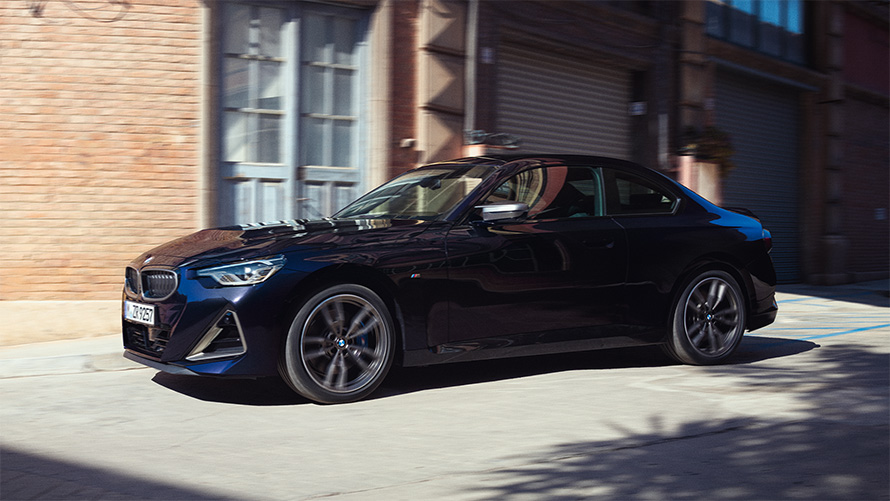 BMW M240i xDrive Coupé, G42, 2021, egy álló autó oldalnézetből BMW M240i xDrive Coupé, G42, 2021, egy raktár előtt álló, Zafírfekete metálfényezésű autó oldalnézetből