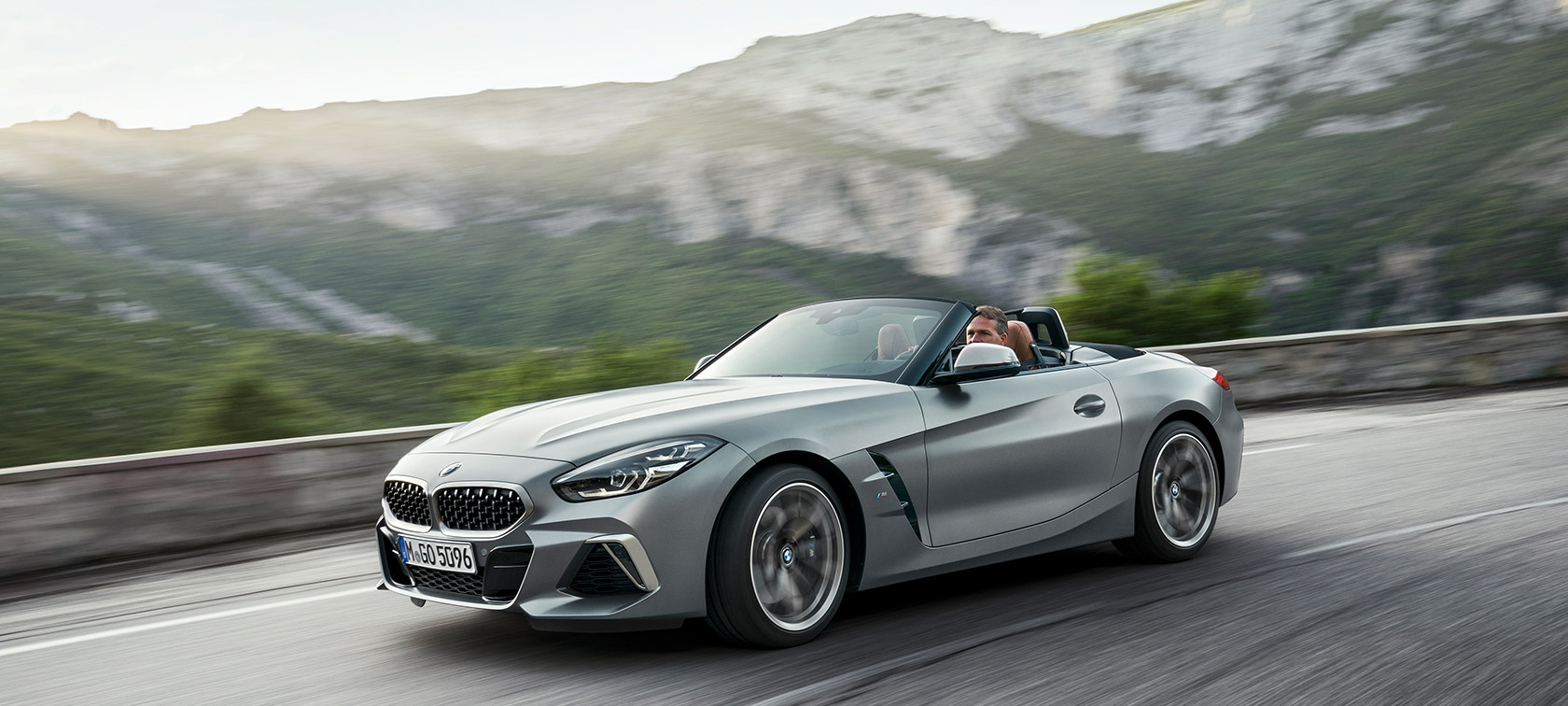 BMW Z4 M40i, G29, egy hegyvidéki úton haladó autó BMW Z4 Roadster M40i, G29, Cabrio, BMW Individual Frozen szürke metál, egy rézsútos elölnézetből látható, mozgó autó hegyvidéki tájjal a háttérben