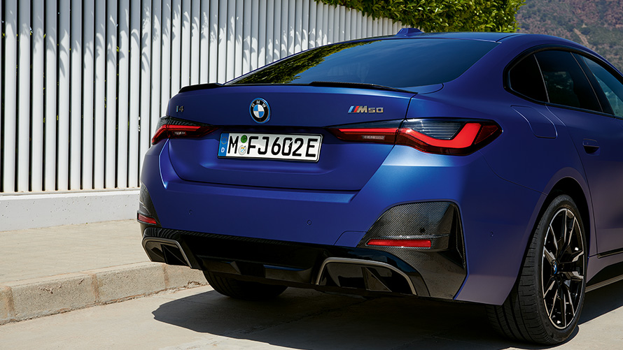 BMW i4 M50, G26, 2021, egy fehér kerítés mellett álló, BMW Individual Frozen Portimao kék metálfényezésű autó rézsútos hátulnézetből