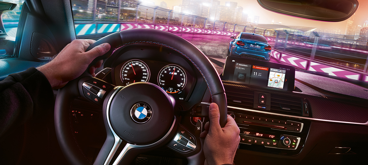 A BMW M2 Competition műszerfala Két, egymással versenyző BMW M2 Competition éjszaka, a kormány mögül nézve.
