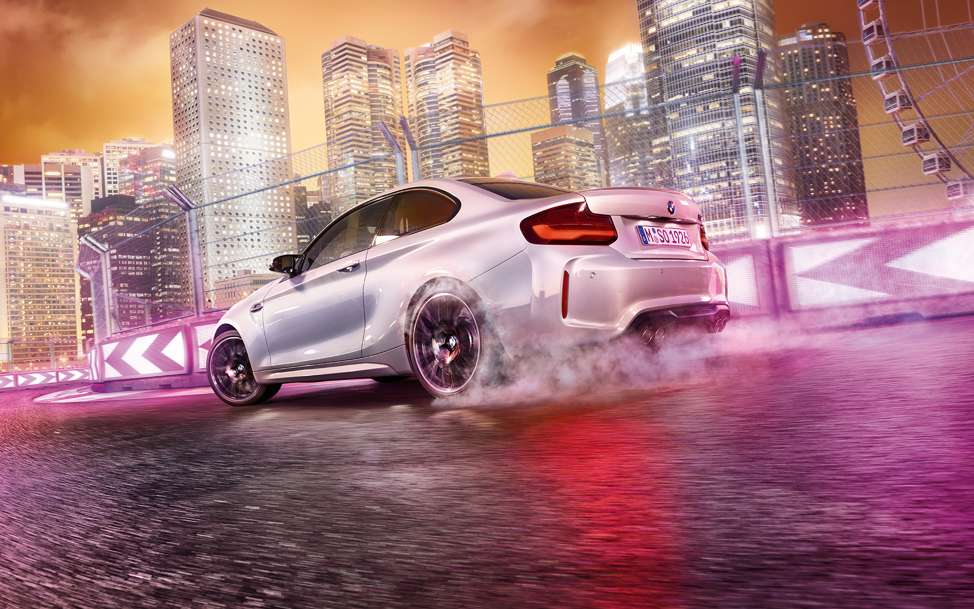 A BMW M2 Competition gyorsít Egy fehér BMW M2 Competition driftel a versenypályán az éjszakai város sziluettjével a háttérben.