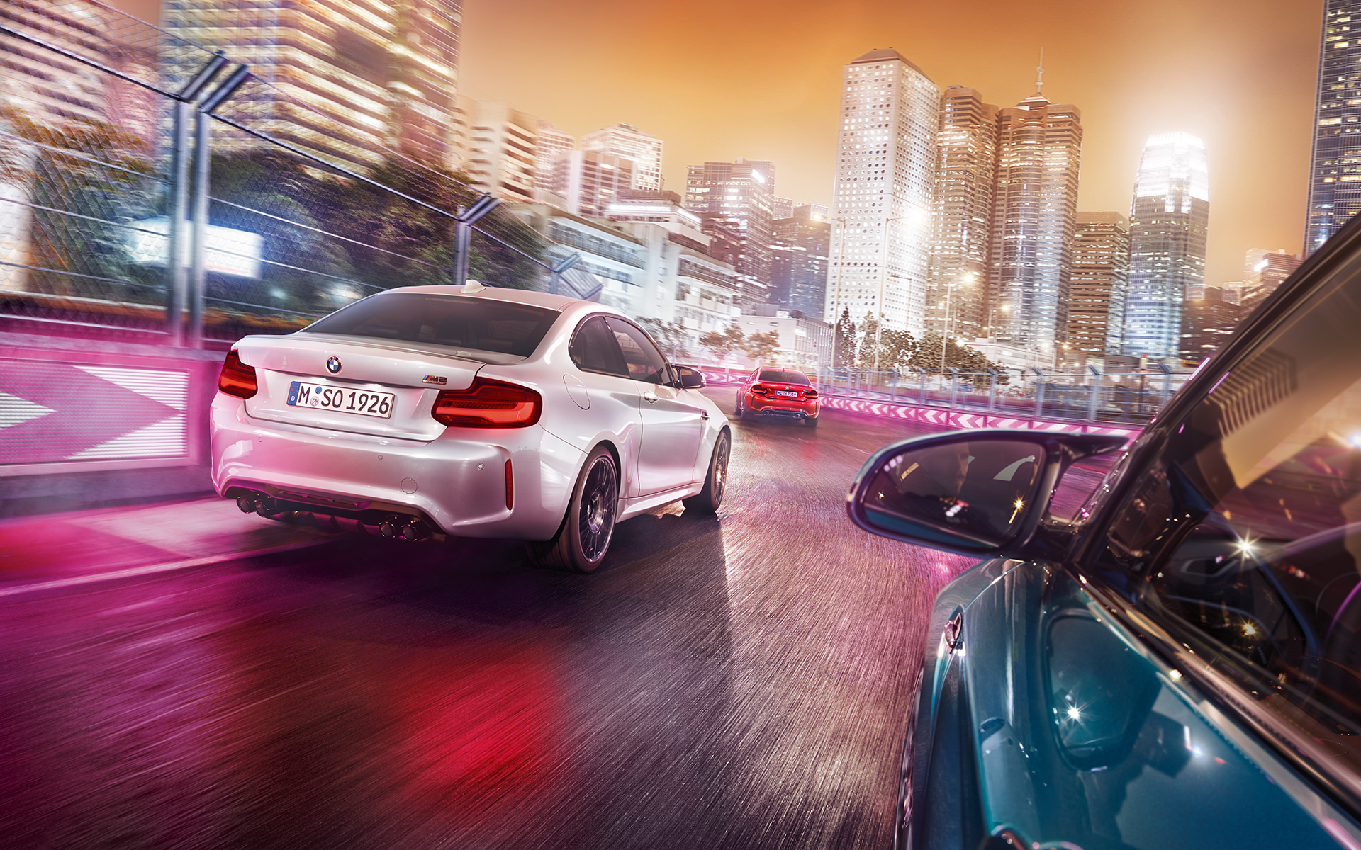 BMW M2 Competition hátulról Három BMW M2 Competition a versenypályán hátulról egy megvilágított háttér előtt
