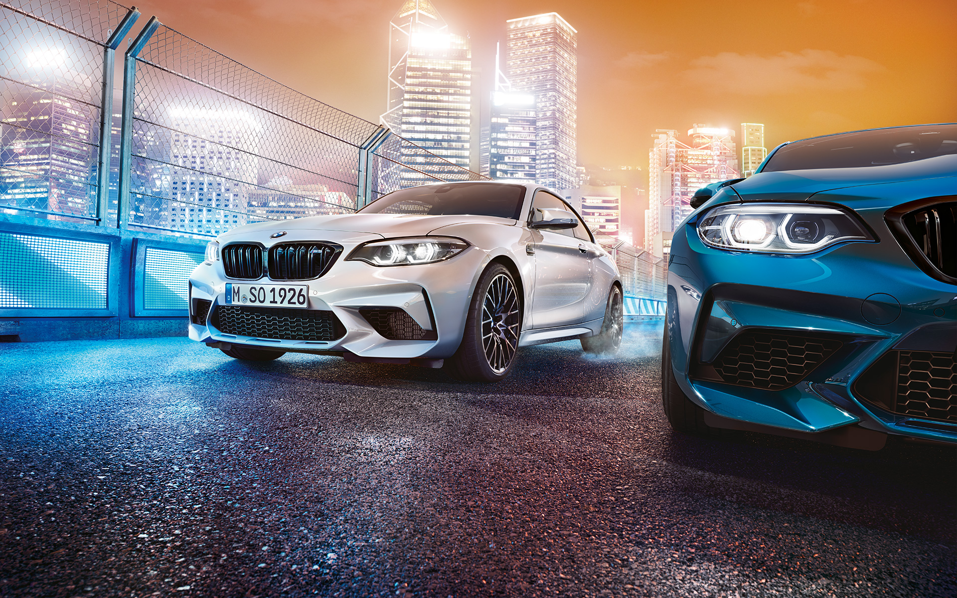 Fehér és kék BMW M2 Competition álló helyzetben Fehér és kék BMW M2 Competition elölről egy éjszakai városi háttér előtt.