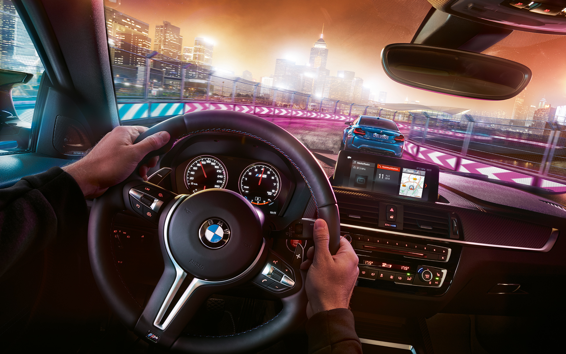 A BMW M2 Competition műszerfala Két, egymással versenyző BMW M2 Competition éjszaka, a kormány mögül nézve.