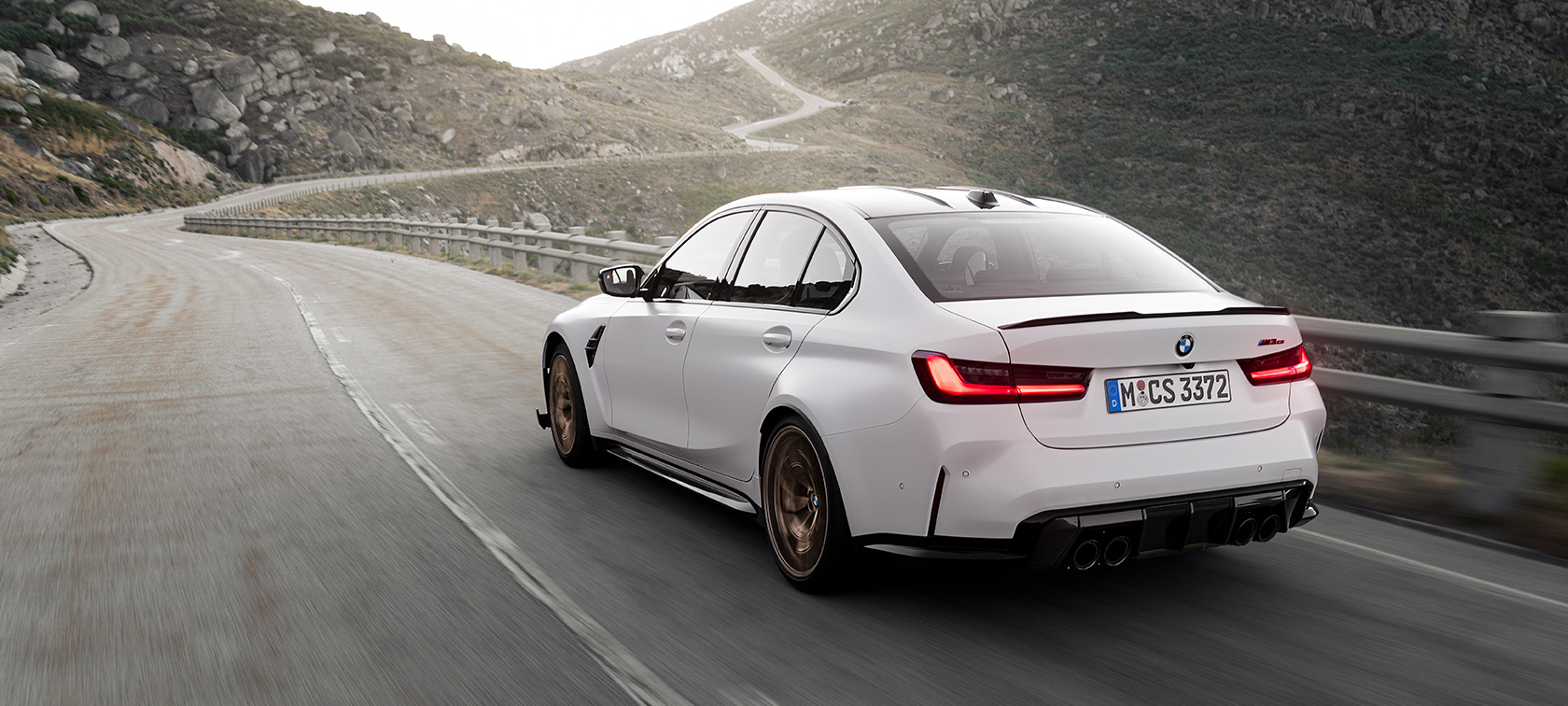 BMW M3 CS, G80, egy mozgó autó rézsútos hátulnézetből BMW M3 CS, G80, egy hegyi úton haladó autó rézsútos hátulnézetből