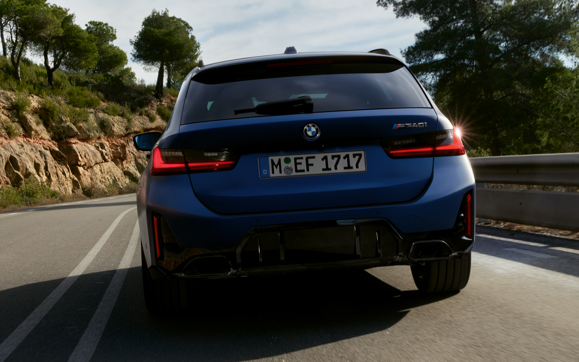 BMW M340i xDrive Touring, G21, egy utcán haladó autó hátulnézetből BMW M340i xDrive Touring, G21, egy utcán haladó, Frozen Tanzanit kék fényezésű autó hátulnézetből