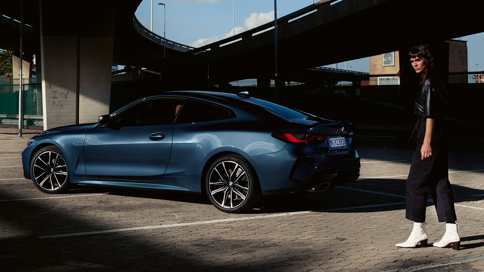 Rézsútos hátulnézet modellel, BMW M440i xDrive Coupé, G22, 2020 BMW M440i xDrive Coupé, Arctic Race kék metál, G22, 2020, egy modell társaságában látható autó rézsútos hátulnézetből