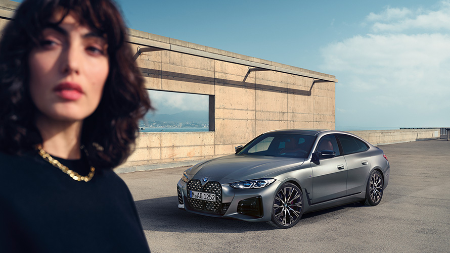 BMW M440i xDrive Gran Coupé, G26, 2021, egy modell társaságában látható autó rézsútos elölnézetből BMW M440i xDrive Gran Coupé, G26, 2021, egy modell társaságában látható BMW Individual Frozen Pure Grey metálfényezésű autó rézsútos elölnézetből