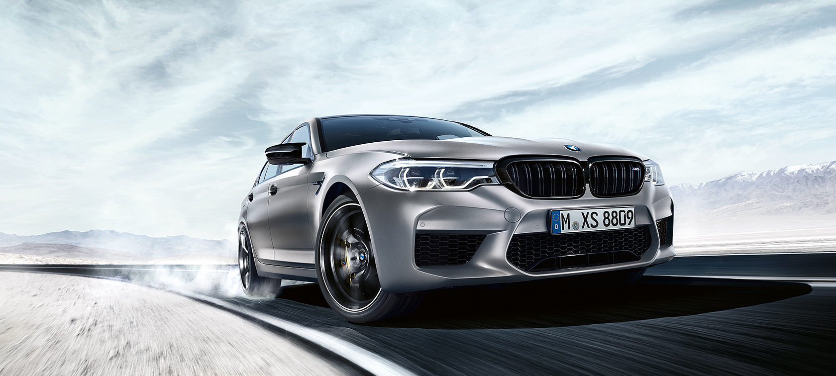 A BMW M5 Competition mozgás közben Egy szürke BMW M5 Competition száguld az autópályán, sivatagos tájjal a háttérben