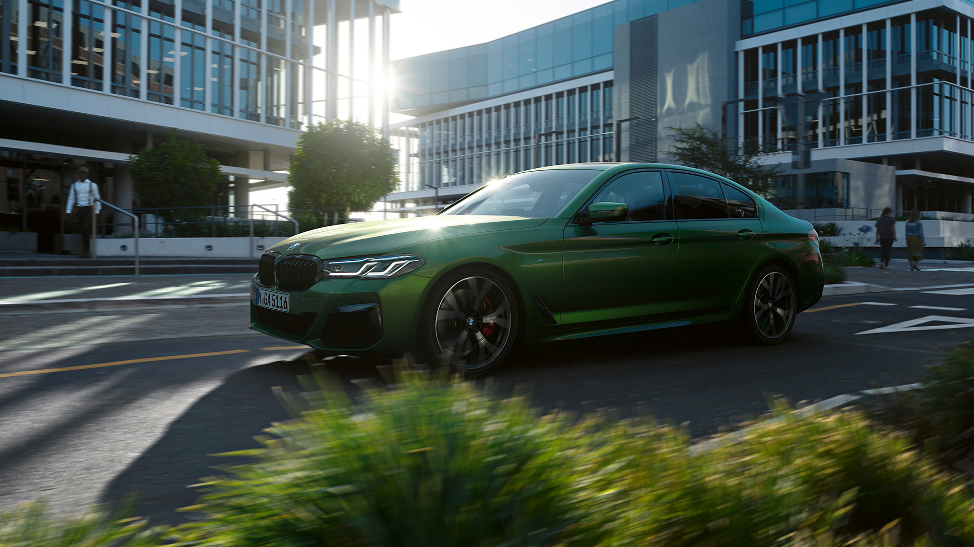 BMW M550i xDrive Limousine, G30 LCI, Facelift 2020, egy mozgó autó oldalnézetből BMW M550i xDrive Limousine, G30 LCI, Facelift 2020, egy belvárosi környezetben haladó BMW Individual Verde Ermes metálfényezésű autó oldalnézetből