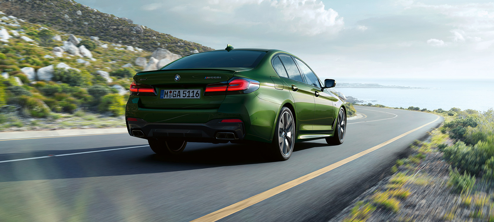 BMW M550i xDrive Limousine, G30 LCI, Facelift 2020, egy mozgó autó rézsútos hátulnézetből BMW M550i xDrive Limousine, G30 LCI, Facelift 2020, egy mozgó BMW Individual Verde Ermes metálfényezésű autó hátulnézetből