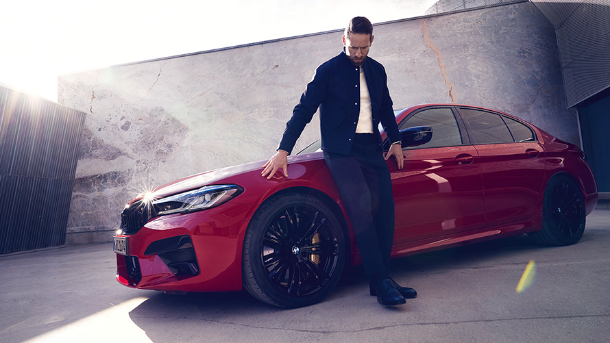 BMW M5 Competition, F90 LCI, Facelift 2020, BMW Individual Imola vörös, egy férfi társaságában látható autó rézsútos elölnézetből