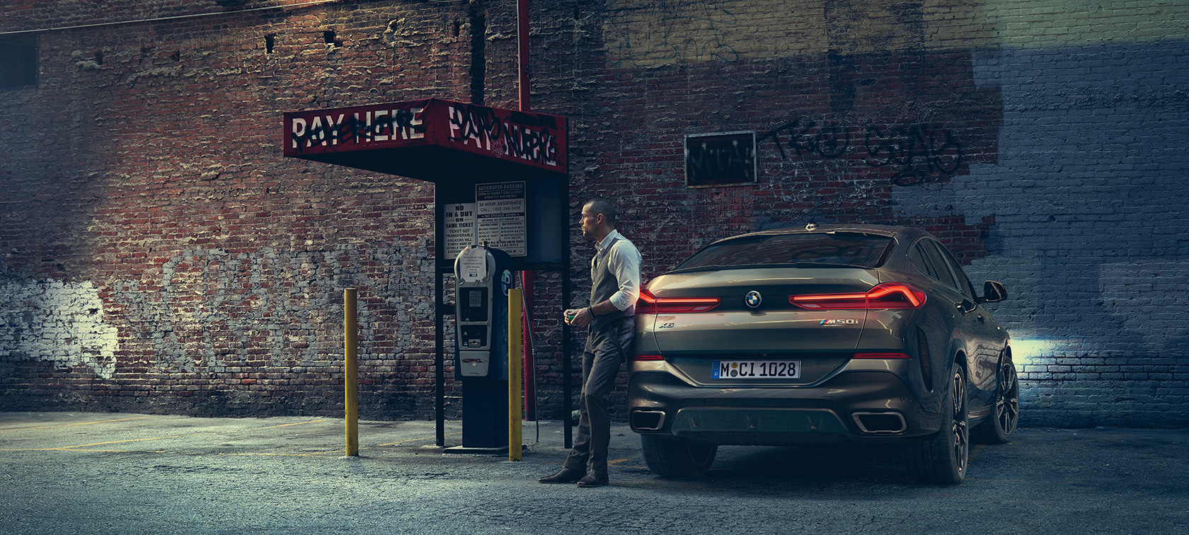A BMW X6 M50i hátsó része. Egy férfi támaszkodik egy BMW X6 M50i farának.