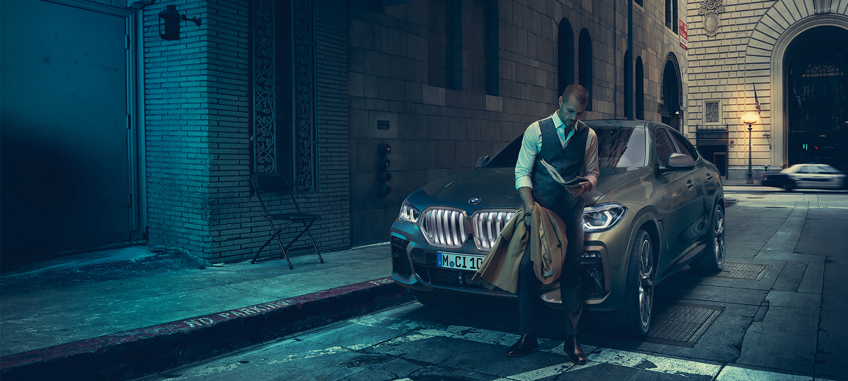 A BMW X6 M50i orr-része. Egy férfi támaszkodik a BMW X6 M50i elejéhez.