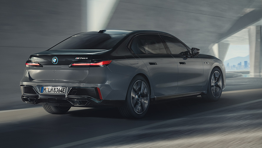 BMW M760e xDrive Limousine, G70, M Performance csomag BMW M760e xDrive Limousine, G70, M Performance csomag, kéttónusú BMW Individual Zafírfekete metál, BMW Individual Dravit szürke metál fényezés, egy utcán haladó autó rézsútos hátulnézetből