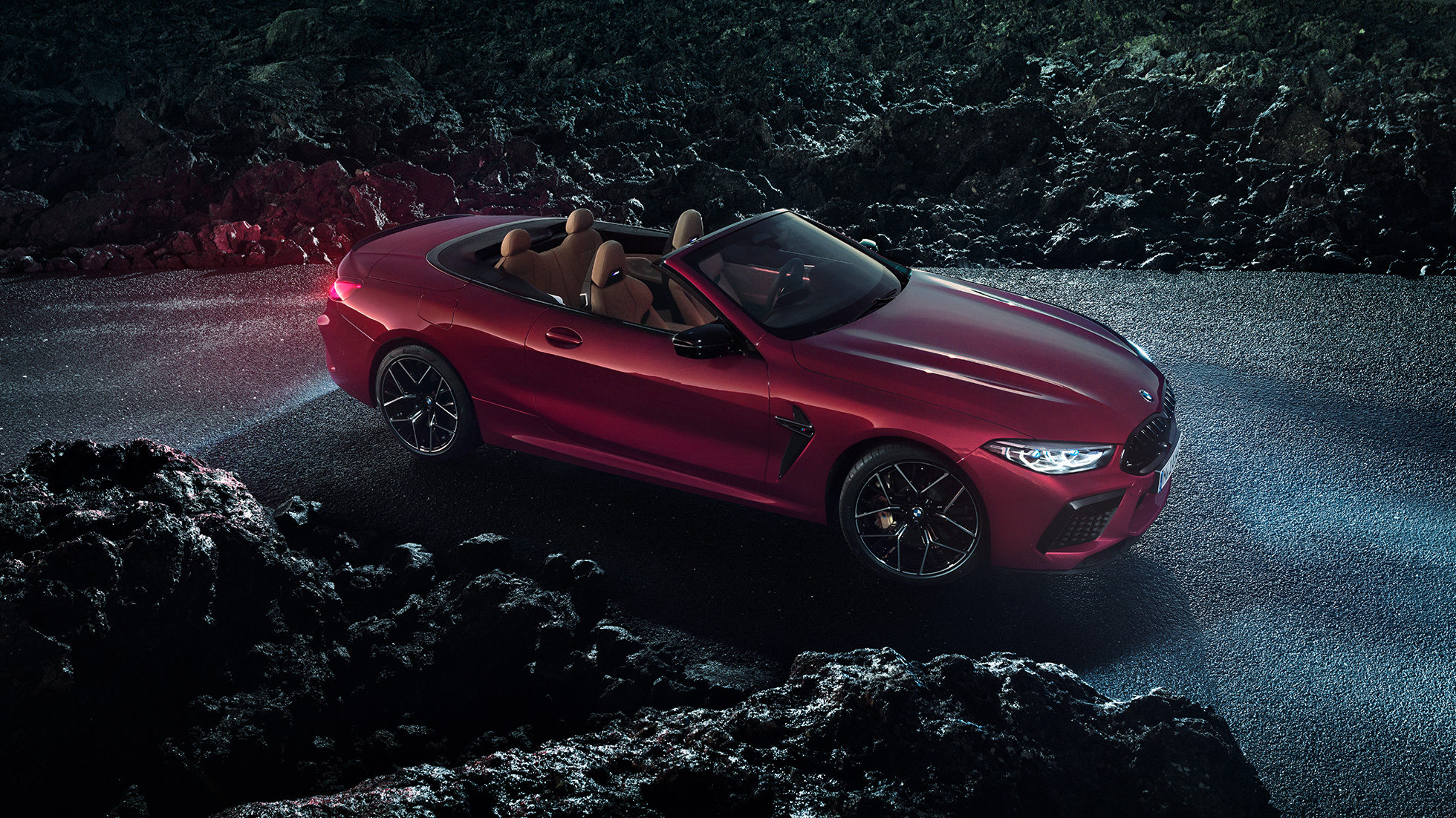 BMW M8 Competition Cabrio, háromnegyedes elölnézet. Egy éjszaka, az aszfalon álló, Motegi vörös metálfényezésű BMW M8 Competition Cabrio háromnegyedes oldalnézetből.