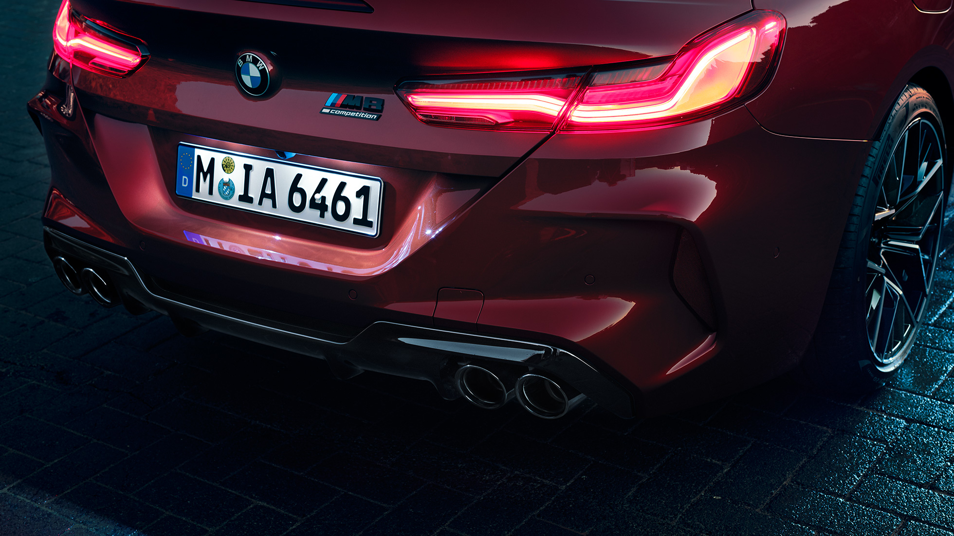 BMW M8 Competition Cabrio, hátulnézet. Egy Motegi vörös metálfényezésű BMW M8 Competition Cabrio fara közelről a LED-es hátsó lámpákkal és az M8 Competition emblémával.