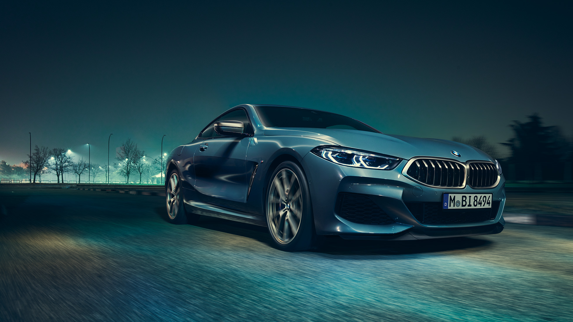 BMW M850i xDrive Coupé, háromnegyedes bal elölnézet. Egy mozgó, Barcelona kék metálfényezésű BMW M850i xDrive Coupé háromnegyedes bal elölnézetből, éjszaka.