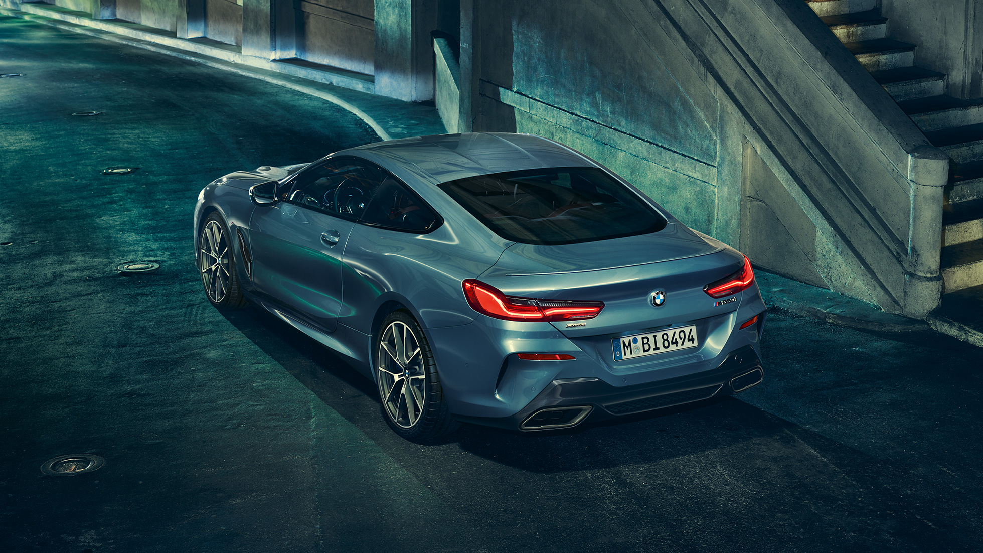 BMW M850i xDrive Coupé, háromnegyedes bal hátulnézet. Egy álló, Barcelona kék metálfényezésű BMW M850i xDrive Coupé háromnegyedes bal hátulnézetből, éjszaka.
