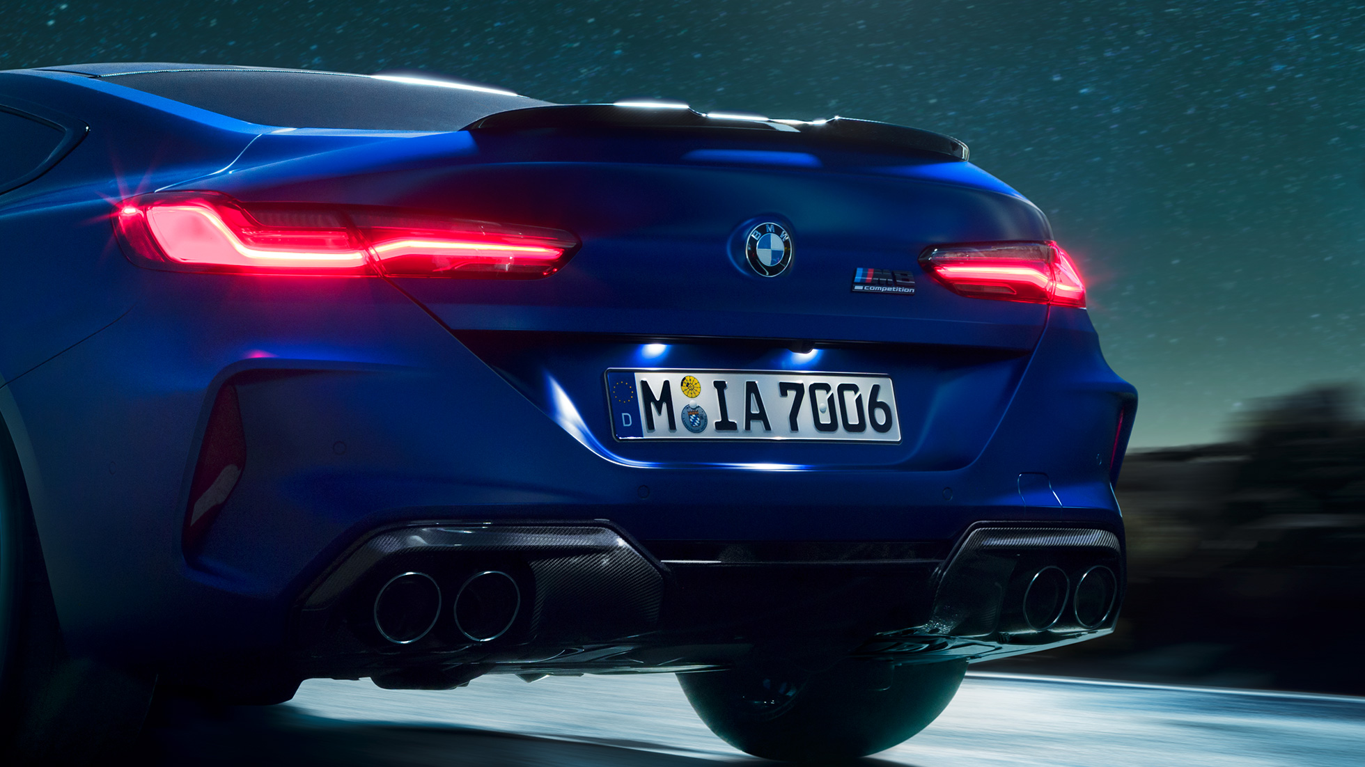 Karbonfekete M diffúzor. Egy Marina Bay kék metálfényezésű, Karbonfekete M diffúzorral ellátott BMW M8 Competiton Coupé közeli hátulnézetből, éjszaka.