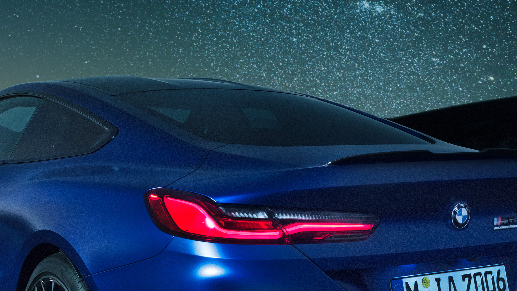 M hátsó légterelő Egy Marina Bay kék metálfényezésű BMW M8 Competition Coupé vállrésze közelről, az M hátsó légterelővel, éjszaka.